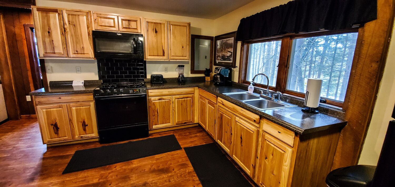 A kitchen with wooden cabinets, a black stove, a sink, and a window with a view of trees.