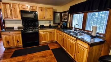 A kitchen with wooden cabinets, a black stove, a sink, and a window with a view of trees.