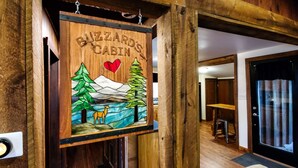 Een houten bord met een berg, bomen en een hert, gelabeld 'BIZZARD'S CABIN'.