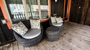 Een overdekte veranda met twee rieten stoelen en een kleine ronde tafel, met kussens met een geometrisch patroon.