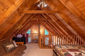 An attic bedroom with wooden beams, a staircase, a sofa, and a bed.