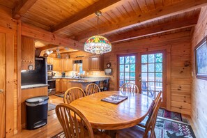 L’intérieur d’un chalet en bois comprend une table à manger, des chaises, un coin cuisine et une grande fenêtre.