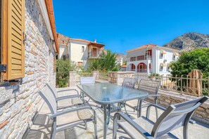 Un patio con una mesa y sillas de vidrio, un muro de piedra y vistas a edificios con tejados rojos.