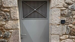 Eine Steinmauer mit einer Metalltür, deren Design ein Kreuz zeigt, und einem kleinen schwarzen Gegenstand an der Wand.