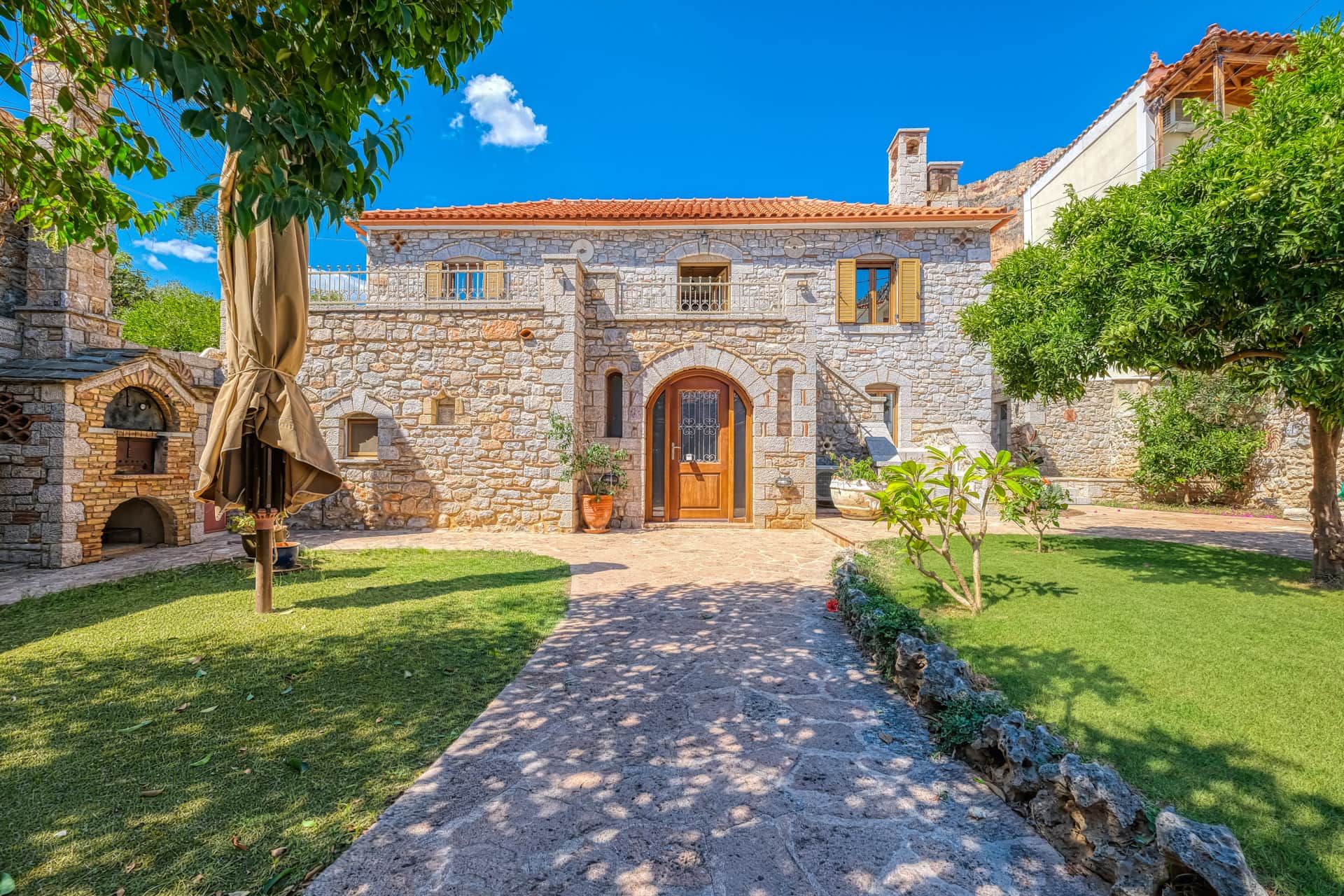 A stone building with a central entrance, a paved pathway leading to it, and a well-maintained lawn.