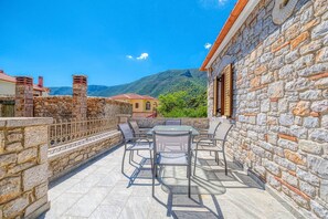 Um pátio externo com paredes de pedra, uma mesa com cadeiras e vista para uma montanha.