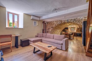 Uma sala de estar acolhedora com um arco de pedra que dá para uma cozinha, mobiliário de madeira e uma janela ampla.