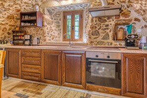 Una cocina con paredes de piedra, armarios de madera, una campana extractora Bosch y una cafetera.