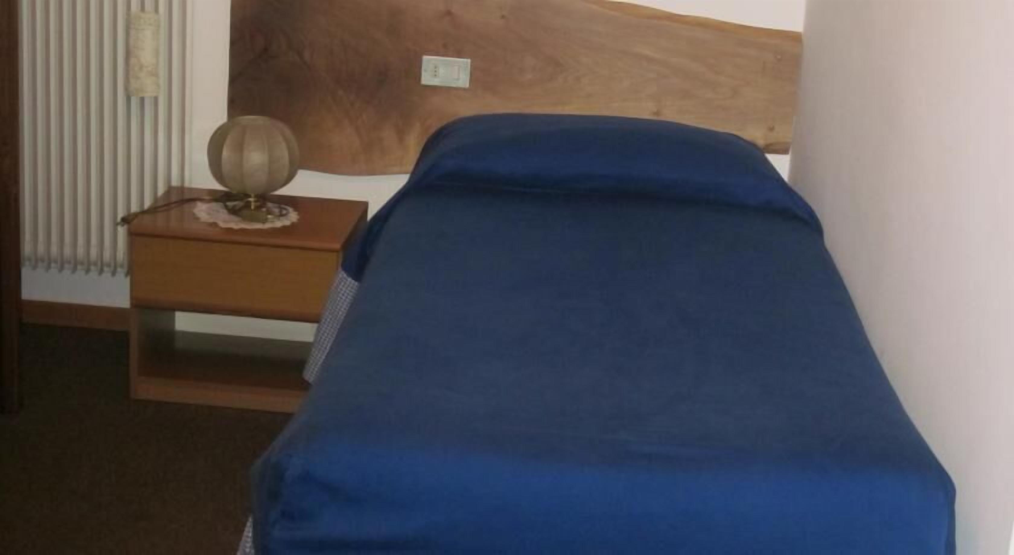 Un letto singolo con materasso blu in una stanza con una testiera in legno e un piccolo comodino anch'esso in legno con una lampada.