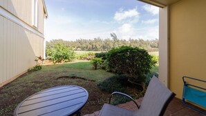 A patio with a table and chairs, a view of a garden, and a building in the background. - Turtle Bay Guava.Price Drop September start at $200 nightly. (Kahuku)
