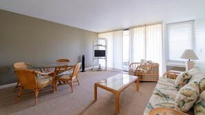 A living room with a glass-top coffee table, wicker chairs, a sofa, and a TV stand. - Turtle Bay Guava.Price Drop September start at $200 nightly. (Kahuku)