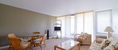 A living room with a glass-top coffee table, wicker chairs, a sofa, and a TV stand.