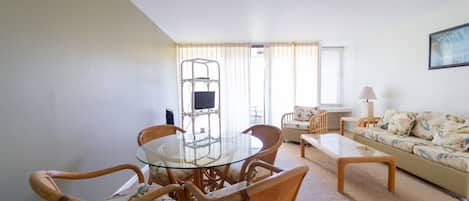 Un coin repas avec une table à plateau de verre, entourée de chaises en osier, d’un canapé et d’une lampe.