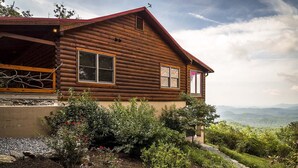 Une cabane en rondins avec un toit rouge, deux fenêtres et une vue sur un paysage montagneux.