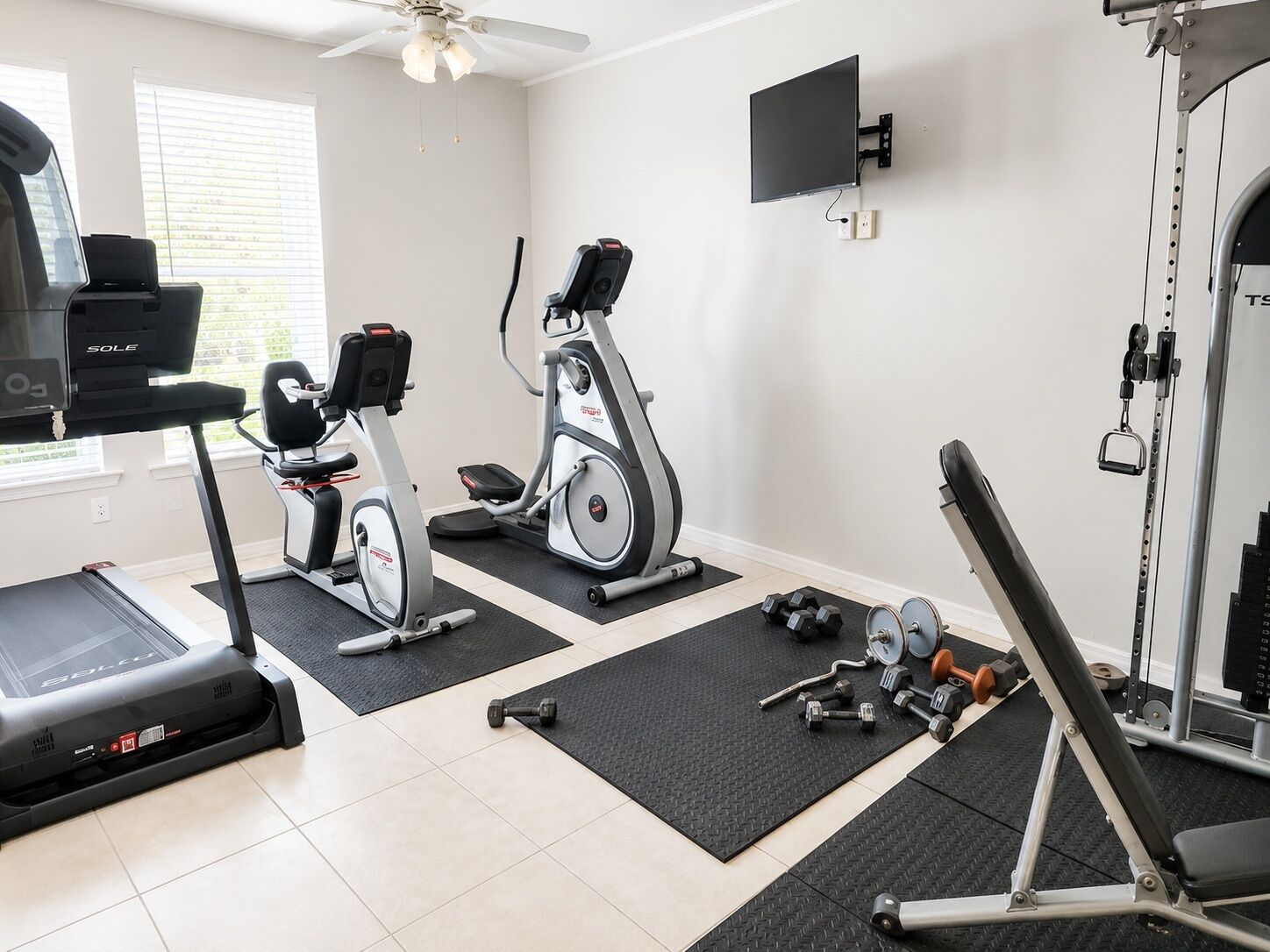 Een huisgym met een loopband, elliptische trainer en gewichtbank.