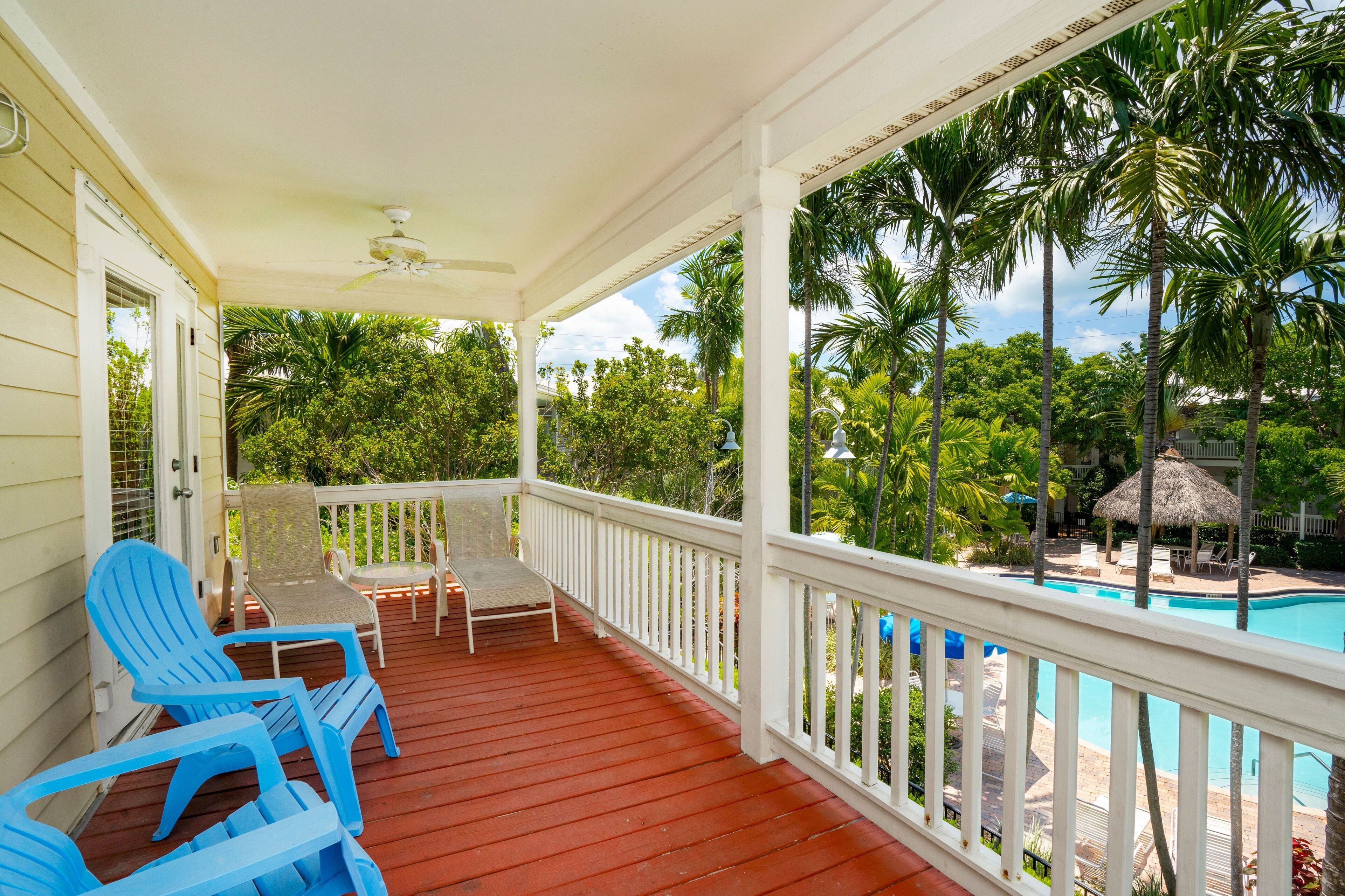 A covered porch with red flooring, white railings, and blue chairs.