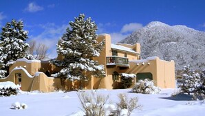 Un edificio cubierto de nieve con un balcón, rodeado de árboles nevados y una montaña al fondo.