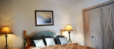 A bedroom with a bed, two bedside tables, a nightstand, a wooden wardrobe, and a framed picture on the wall.