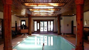 Una piscina interior con vigas y columnas de madera, rodeada de suelo y paredes de azulejos.