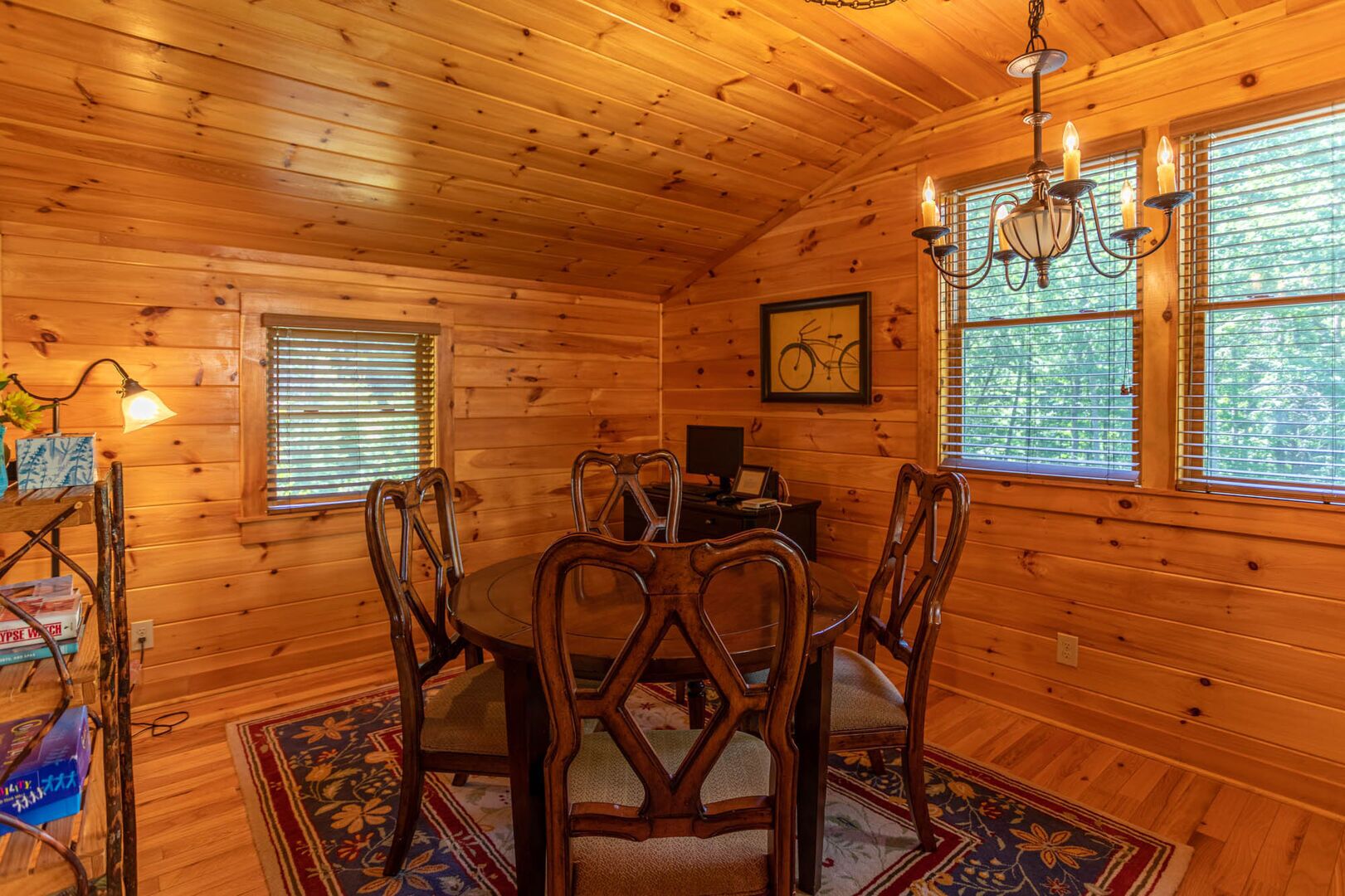 A wooden cabin interior with a dining table, chairs, a chandelier, and framed artwork on the walls.