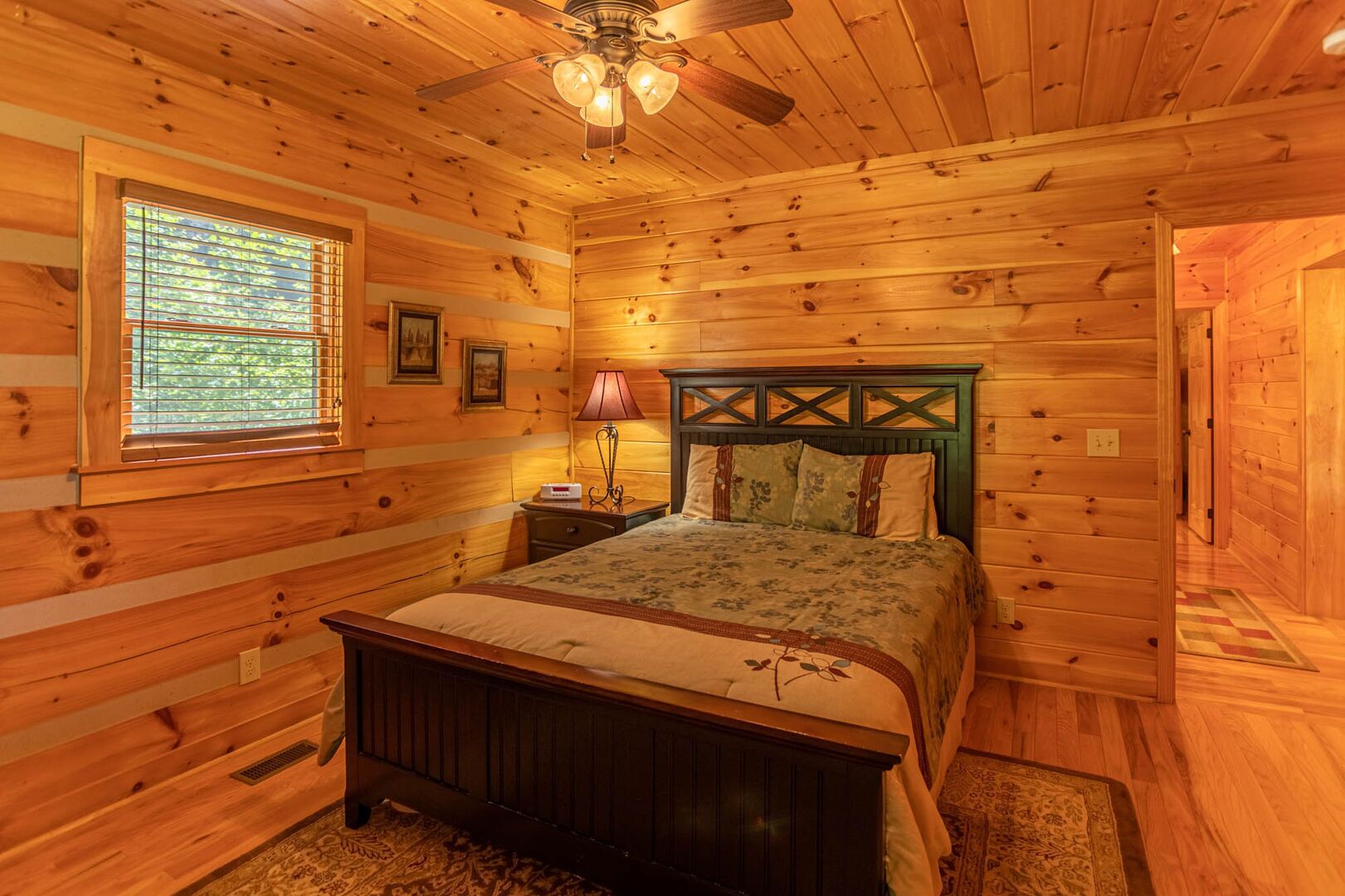 A wooden cabin bedroom with a bed, a nightstand, a lamp, and a ceiling fan.