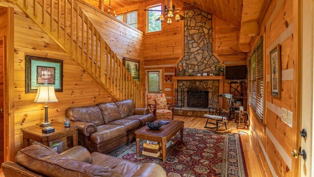 A cozy log cabin interior with a stone fireplace, leather furniture, and a staircase. - A Positive Outlook -10 mins to ASU, Hot Tub - Pool Table - Corner Jacuzzi (Vilas)