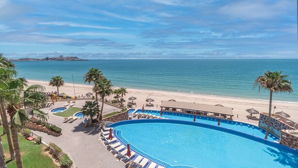 A resort with a large swimming pool, beach, and ocean view.