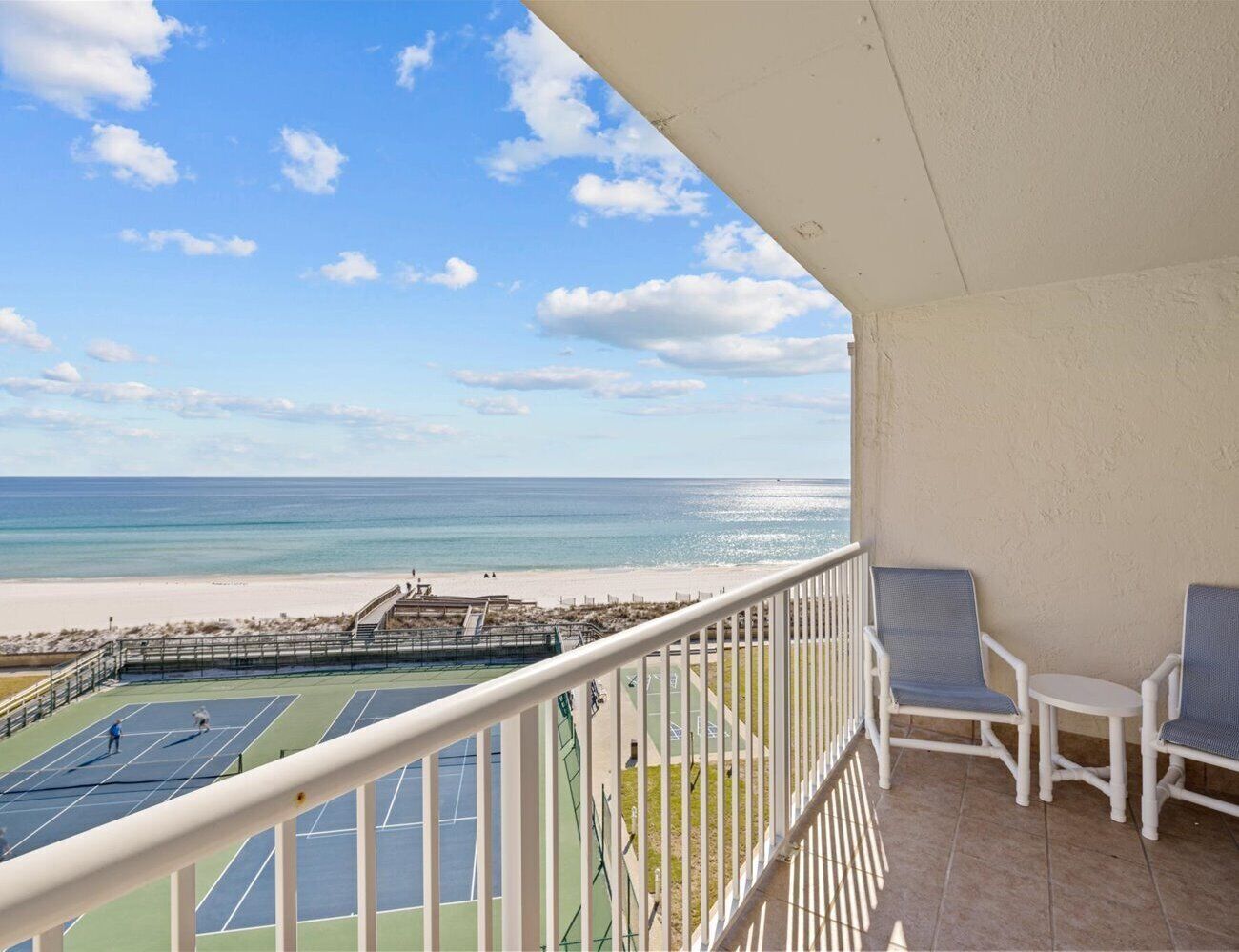 A balcony with a view of a beach and tennis courts.