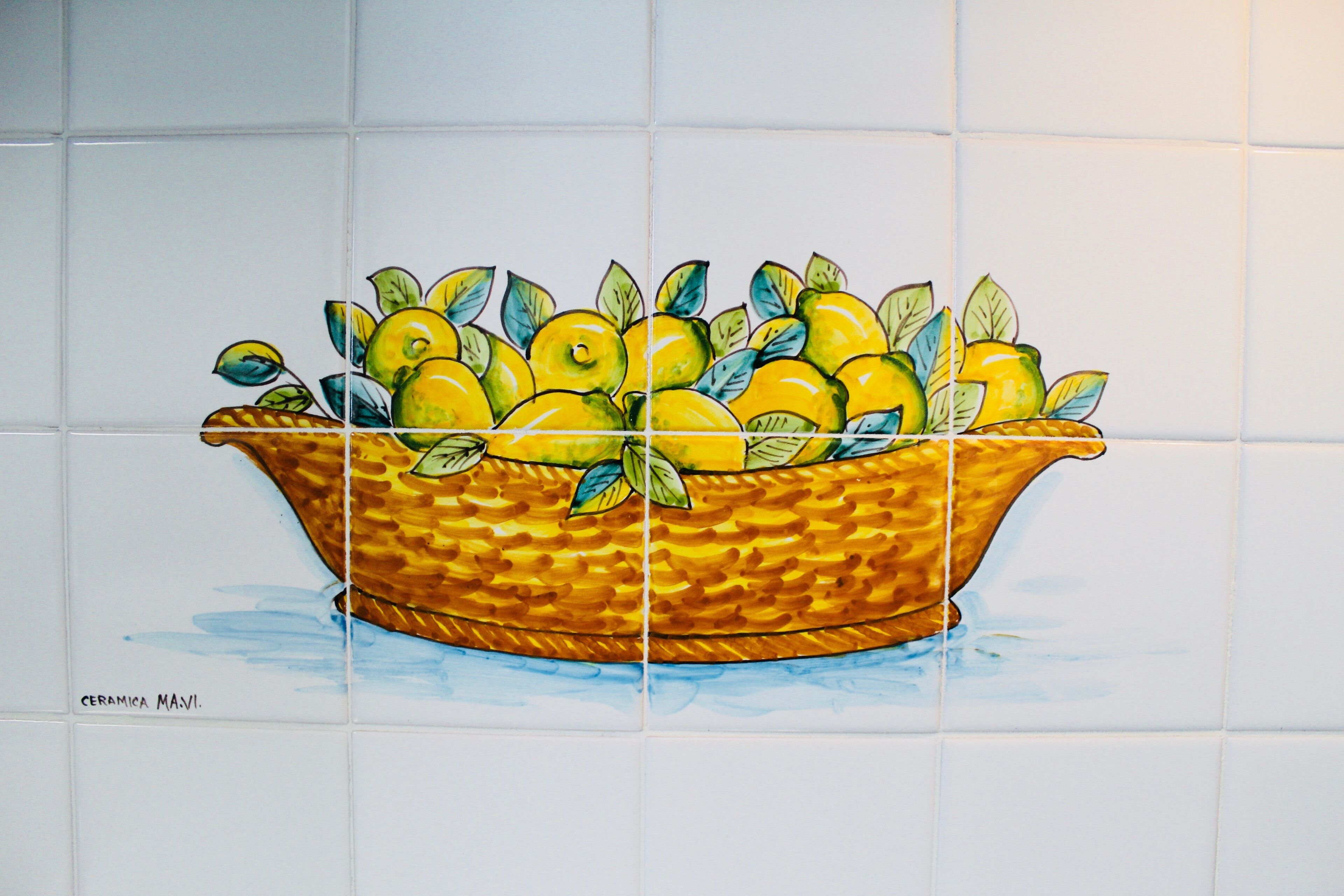 Pared de azulejos con una cesta de limones y hojas.