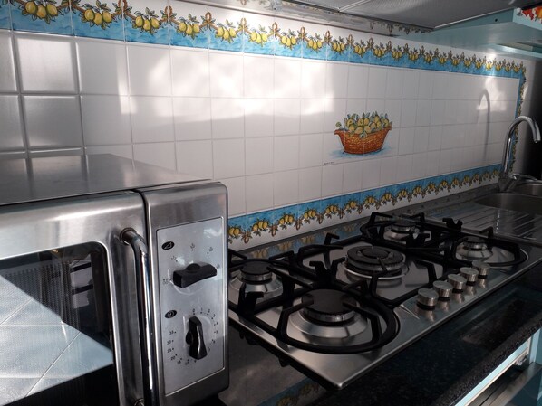 A kitchen with a gas stove, a toaster, and a tiled backsplash with a fruit pattern.