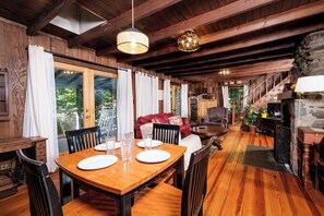 Un comedor de madera con una mesa dispuesta para cuatro, una escalera que sube a un nivel superior y una chimenea de piedra.