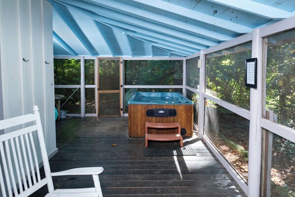 Un espacio al aire libre cubierto con jacuzzi, terraza de madera y paredes de vidrio que ofrecen vistas al follaje circundante.