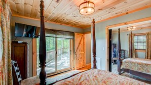 Ein Bett mit Baldachin, ausgestattet mit einer gemusterten Bettdecke, ein an der Wand befestigter Fernseher und eine Holzbalkendecke.