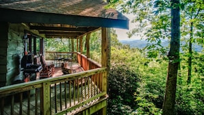 Eine Holzhütte mit Veranda, Sitzgelegenheit im Freien und Blick auf eine bewaldete Landschaft.