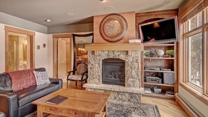 Ein Wohnzimmer mit Kamin aus Stein, einer Ledersofa, einem Couchtisch aus Holz und einem Fernseher, der über dem Kamin angebracht ist.
