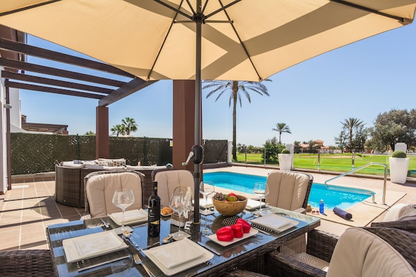 An outdoor dining area with a pool view, wicker furniture, and a table set for a meal.