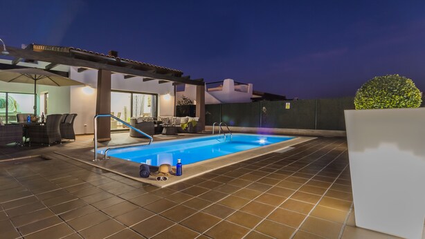 An indoor swimming pool with a tiled floor, a pool ladder, and a seating area with chairs and a table.