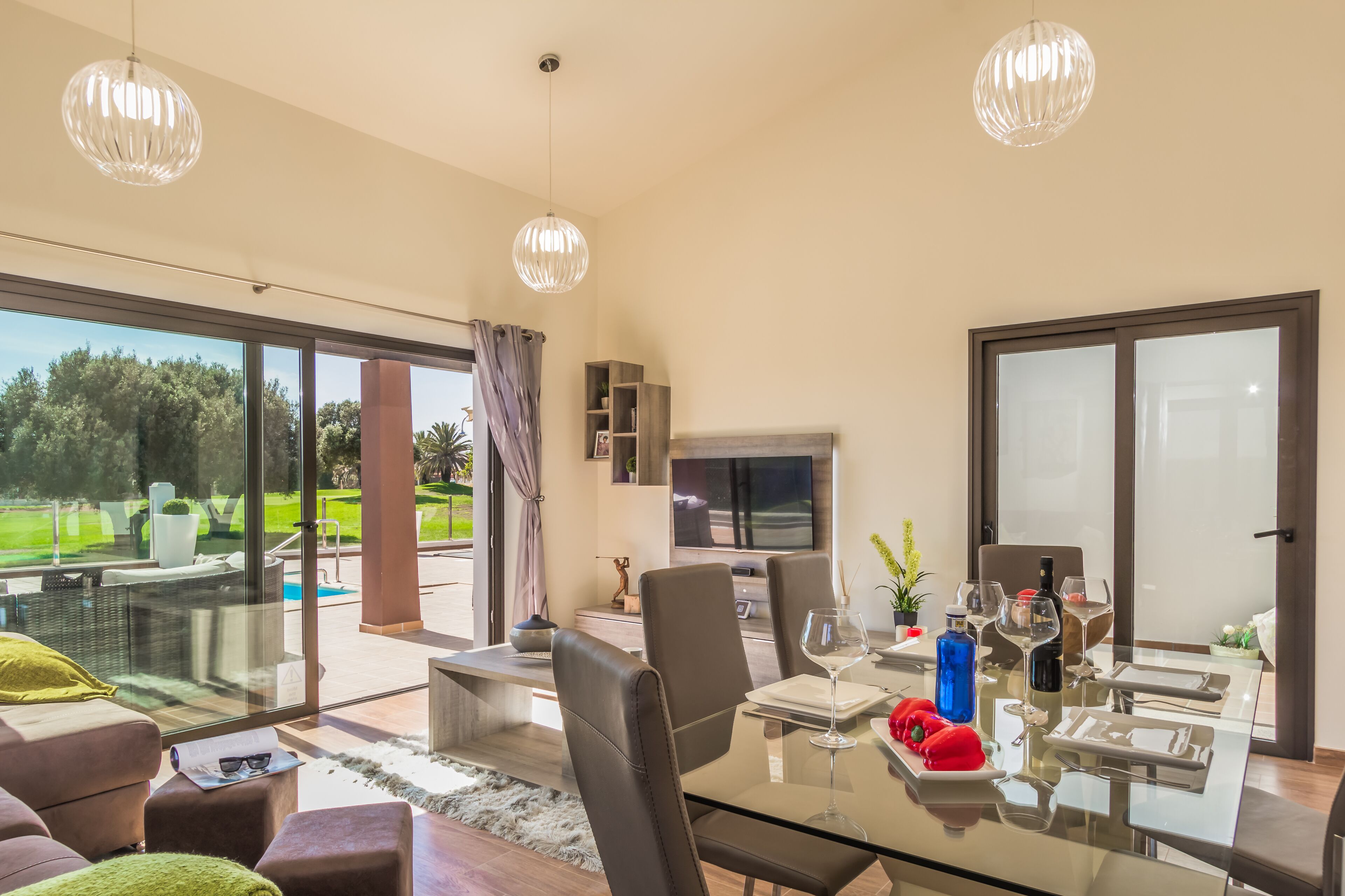Un comedor moderno con una mesa de vidrio, sillas de cuero y vistas a una piscina y follaje exterior.