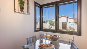 A dining area with a glass table, two chairs, a plate of croissants, a bowl of fruit, and two glasses of orange juice.