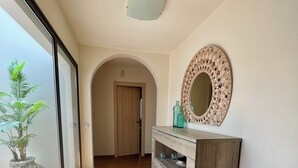 A hallway with a wooden floor, a glass door leading to a balcony, a wooden cabinet with a mirror, and a plant on the balcony.