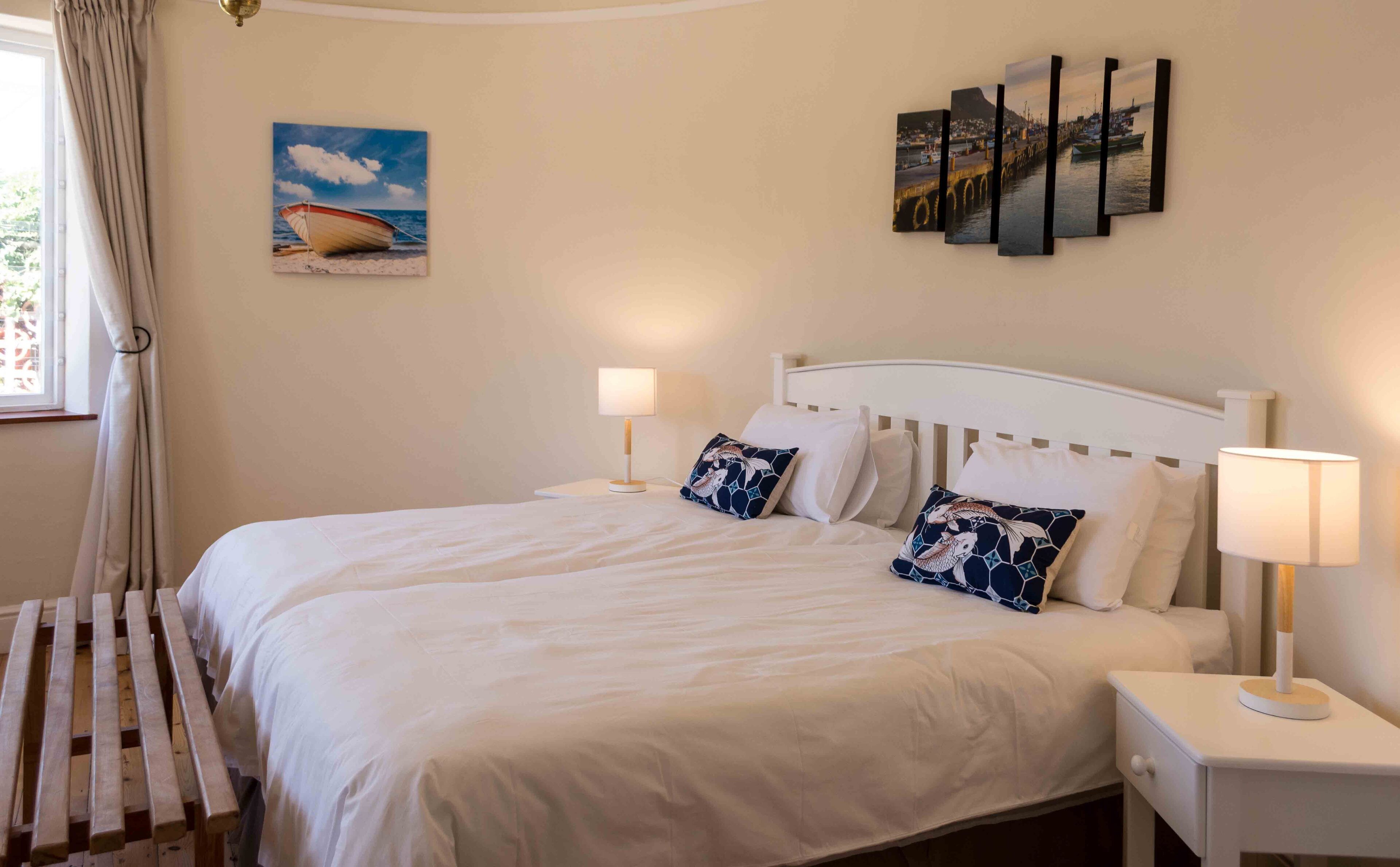 A bedroom with a large bed, two bedside tables with lamps, a window with curtains, and wall art.