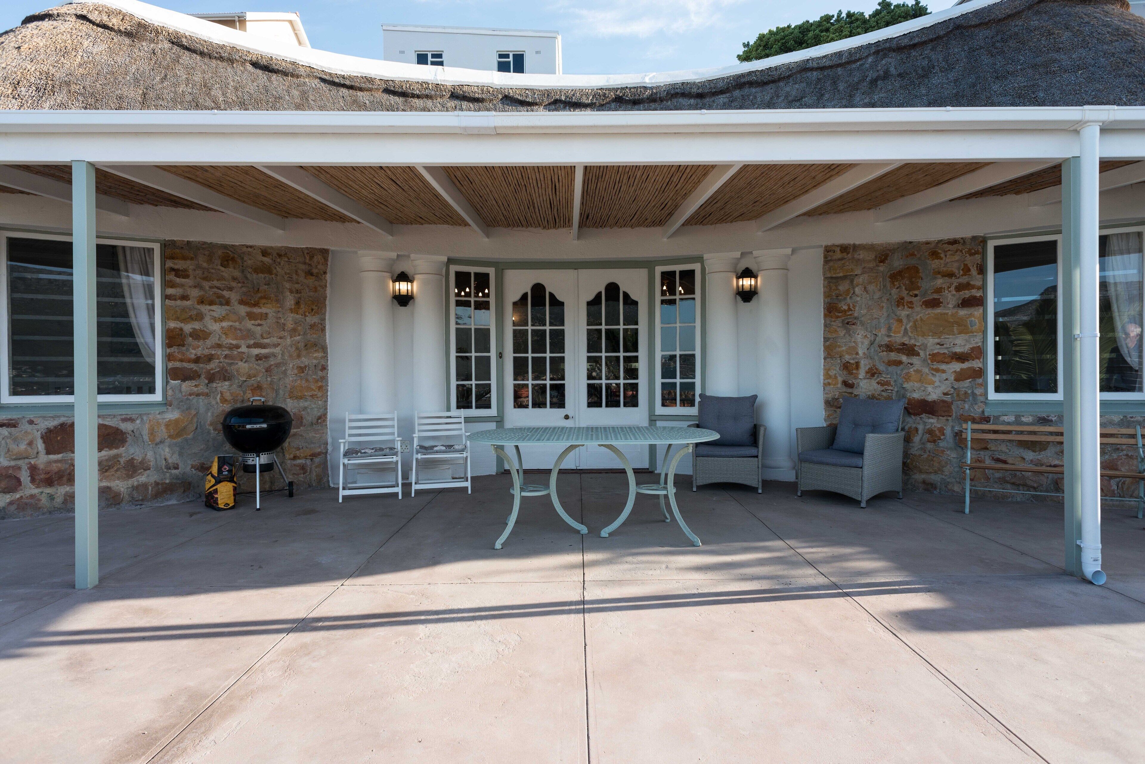 A covered outdoor patio with a stone wall, a table, chairs, and a grill.