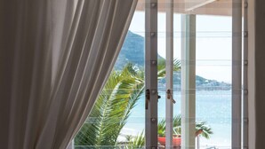A window with a view of a beach, a curtain, and a potted plant. - Sea Cottage - House - spectacular sea views (Cape Town)