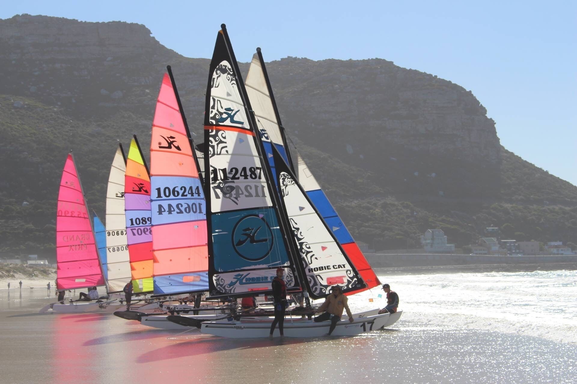 A row of colorful sailboats on a beach with a mountainous backdrop.