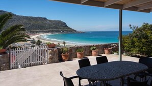 A terrace with a view of a beach and ocean, featuring a table and chairs, potted plants, and a white fence. - Sea Cottage - House - spectacular sea views (Cape Town)