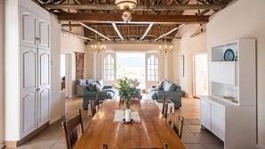 A spacious dining area with a wooden table, surrounded by chairs, and a large window providing a view of the outdoors. - Sea Cottage - House - spectacular sea views (Cape Town)