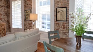 A dining area with a wooden table, chairs, a vase with flowers, and a brick wall. - Local Culture themed Historic luxury condo, 2 blocks from French Quarter (New Orleans)