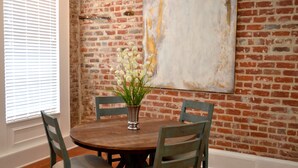 A dining area with a brick wall, a round wooden table, and two chairs. - Local Culture themed Historic luxury condo, 2 blocks from French Quarter (New Orleans)