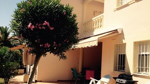 A patio with two white lounge chairs, a small tree with pink flowers, and a barbecue grill.