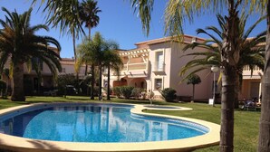 A swimming pool with a curved edge, surrounded by well-maintained grass and palm trees.